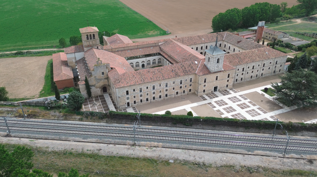 Panorámica aérea general del Monasterio de San Isidro de Dueñas, con las vías del tren frente al edificio.