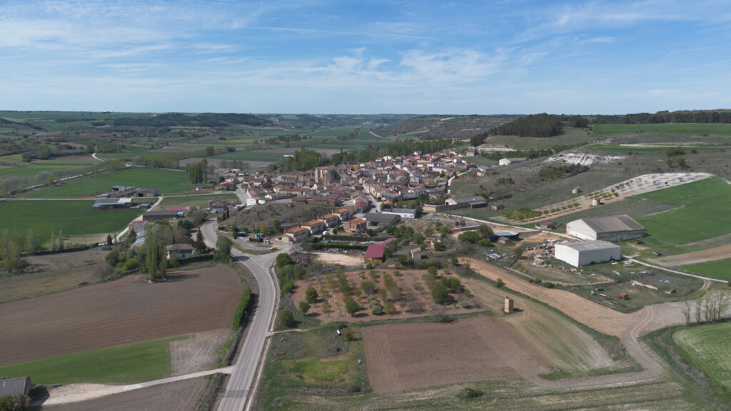 Panorámica aérea general de Castrillo de Don Juan, asentado en la ladera de los páramos, cuyo desarrollo se aprecia al fondo.