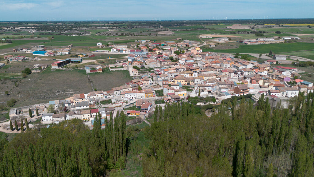 Panorámica aérea de Hérmedes de Cerrato, asentado sobre la ladera del páramo. En primer término la frondosa arboleda que puebla la vega del Arroyo Maderón.
