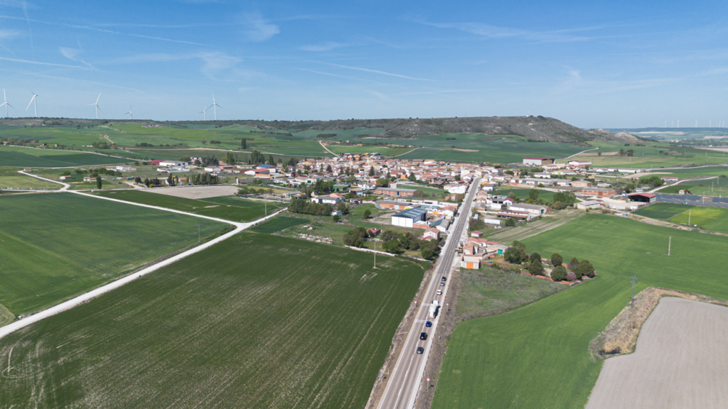 Panorámica aérea de Villaviudas, rodeado de campos de cultivo. Al fondo los páramos, sobre los que se alzan aerogeneradores.