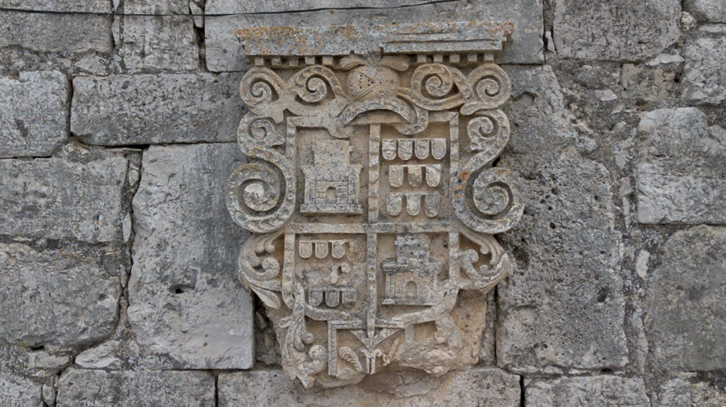 Escudo de armas de una de las vasas blasonadas de Valdecañas de Cerrato. Tiene cuatro cuerpos en los que se alternan castillos y estandartes, todo ello coronado por un yelmo mirando a izquierda.