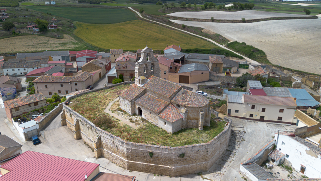 Panorámica aérea general de la iglesia de San Juan Bautista de Valdeolmillos. Destaca su espadaña y la cabecera con canecillos románicos.