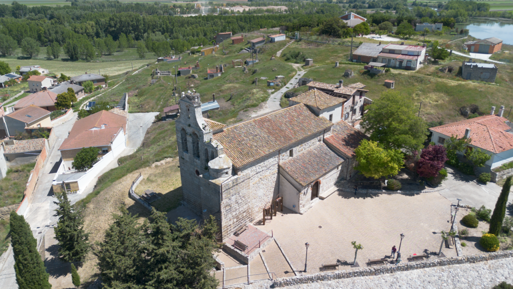 Panorámica aérea de la iglesia de la Asunción de Reinoso de Cerrato. Destaca la espadaña de la iglesia y tras la iglesia las puertas de las bodegas.