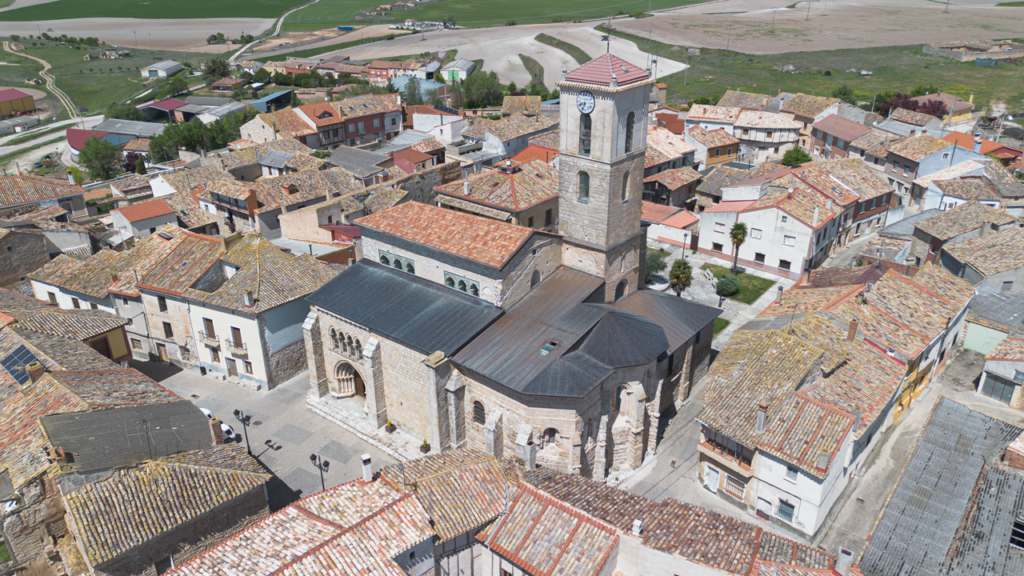 Panorámica aérea de la iglesia de San Miguel Arcángel de Vertavillo. Destaca su alta torre y su portada tardorrománica con arquivoltas y capiteles decorados. Se aprecia también la apretada trama urbana de calles estrechas.
