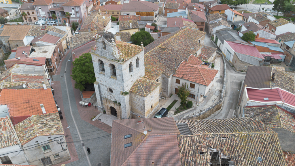 Panorámica aérea de la iglesia de Nuestra Señora de la Asunción de Villaviudas. Hay un gran nido de cigüeña en lo alto de la torre, apoyado en la espadaña.