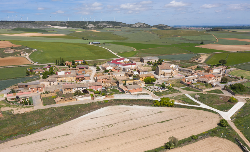 Panorámica aérea de Villodre rodeado de campos de cultivo. Al fondo los páramos con numerosos molinos eólicos.