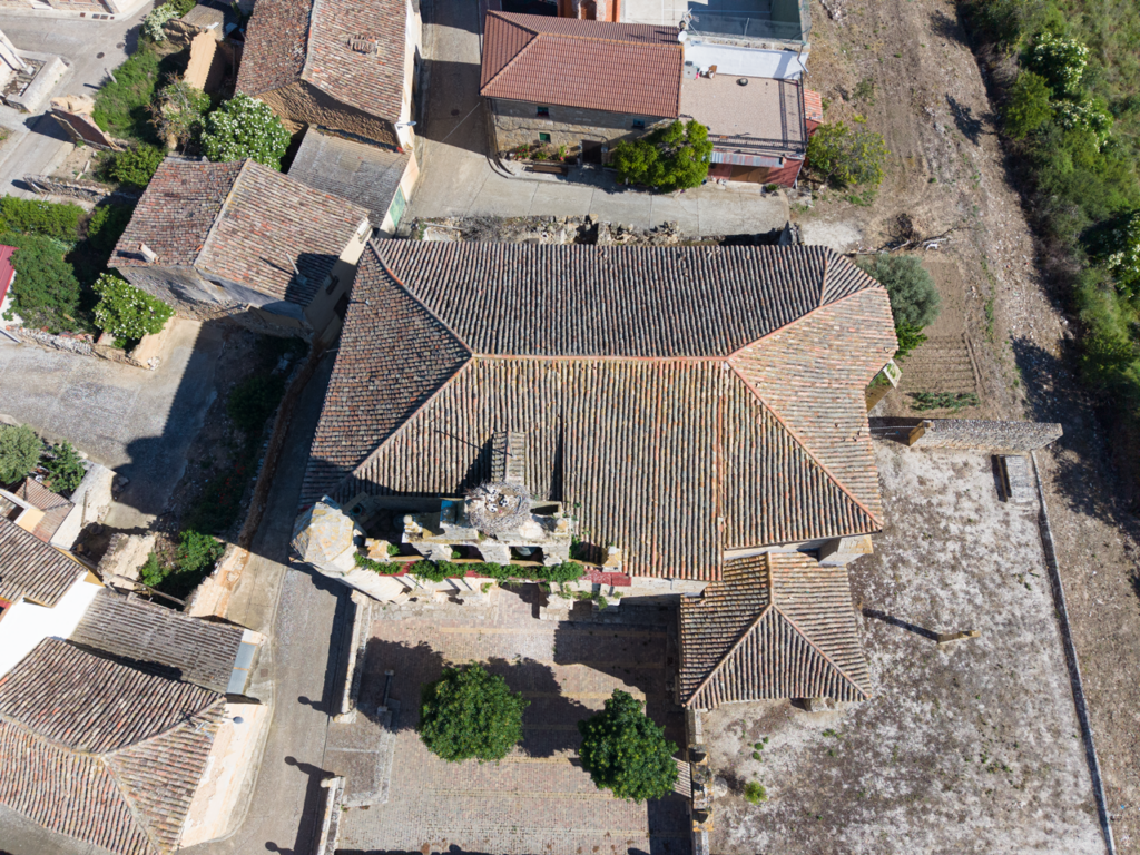 Panorámica aérea picada de la iglesia de Santa Eugenia de Villalaco. Sobre la espadaña hay un nido de cigüeña con cuatro polluelos.