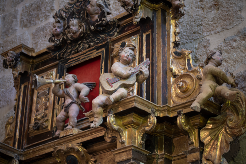 Detalle de uno de los retablos barrocos de la iglesia de San Miguel de Tariego de Cerrato. Sobre la cornisa del atrio hay varios querubines tocando incstrumentos musicales, como la guitarra.
