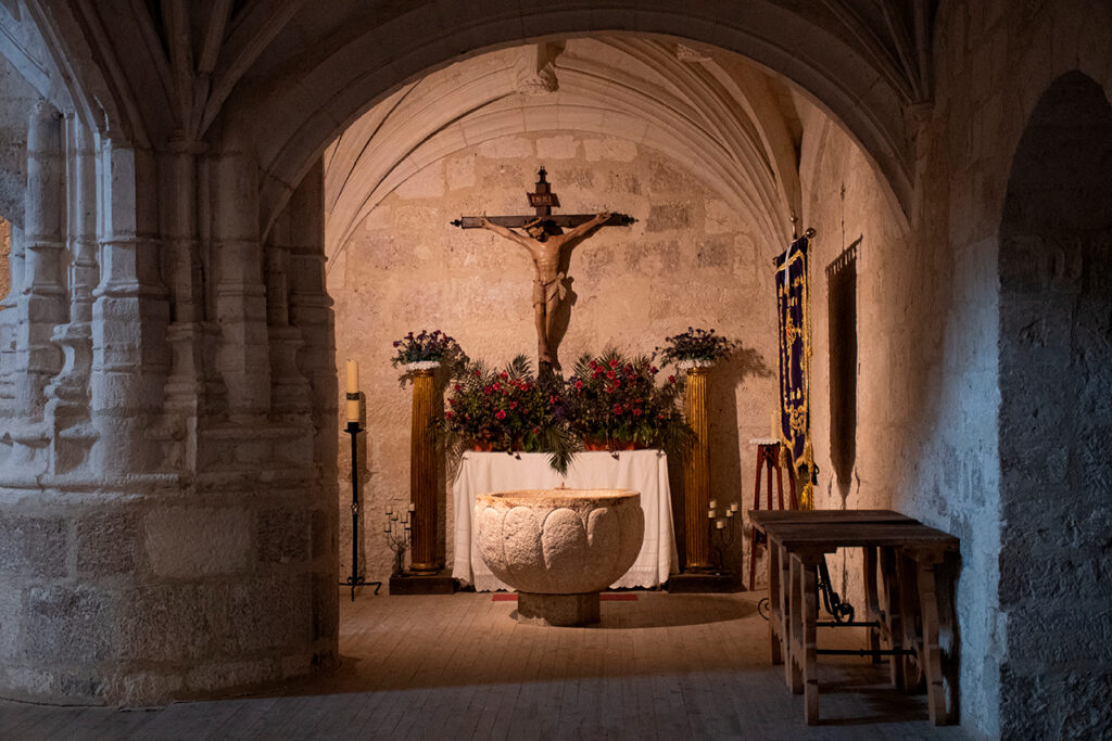 Pila bautismal románica de la iglesia de San Millán de Baltanás. Al fondo en la pared, un Cristo Crucificado.