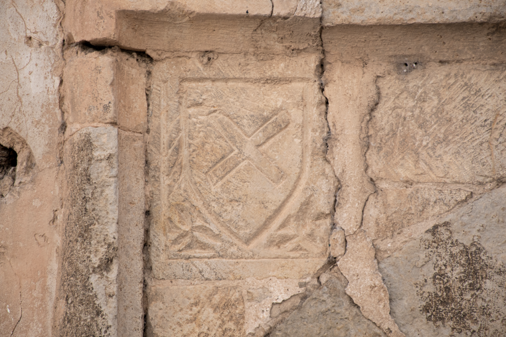 Detalle de una portada blasonada de torquemada. En primer término un escudo de armas con una cruz en aspa.