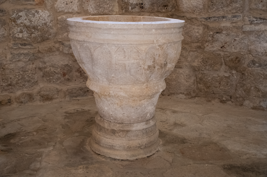 Pila bautismal de la iglesia de San Juan Bautista de Valdeolmillos. Decorada con arquillos, pudiéndose apreciar una cruz dentro de uno de ellos.