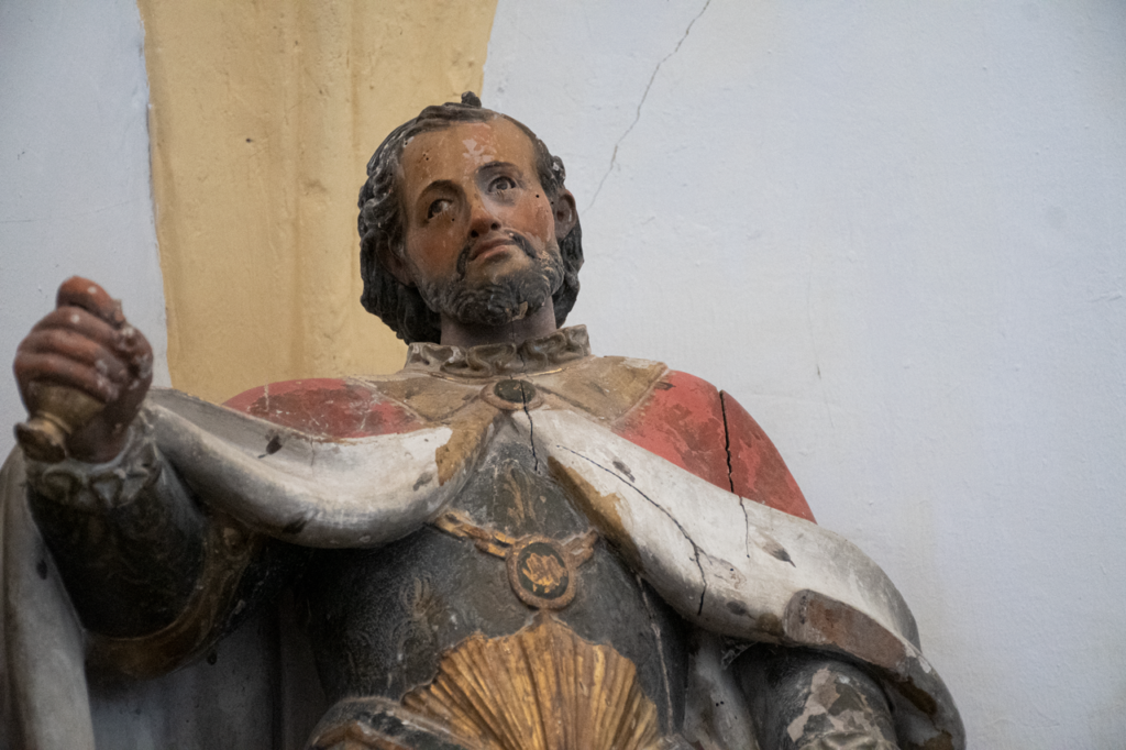 Detalle de una escultura de San Fernando. Viste armadura, capa de armiño y empuña una espada de la que solo queda la empuñadura.