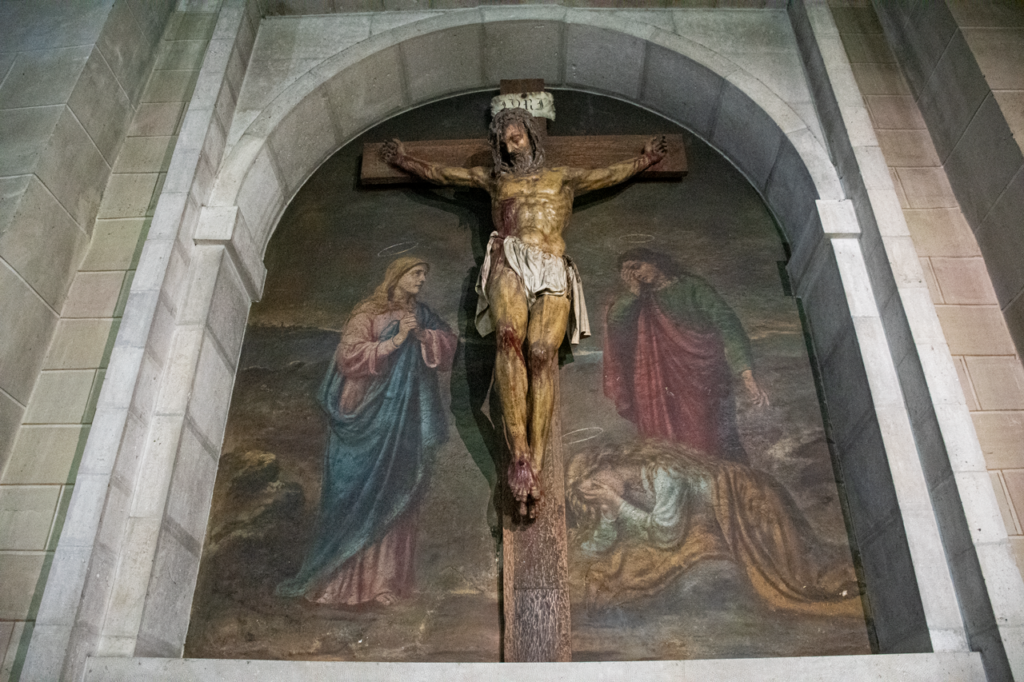 Escultura de Cristo crucificado en una hornacina. En la pared se representan pintados a la Virgen María, San Juan y María Magdalena en el monte Gólgota.