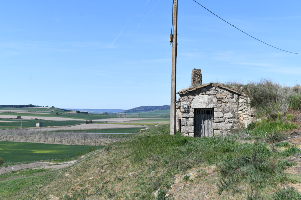 En primer plano la entrada de una de las bodegas de Vertavillo, y al fondo el valle con campos de cultivo y los cerros de los páramos.
