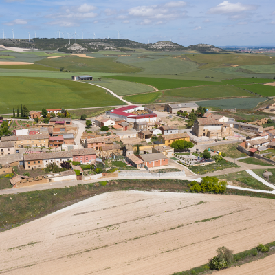 Panorámica aérea de Villodre rodeado de campos de cultivo. Al fondo los páramos con numerosos molinos eólicos.